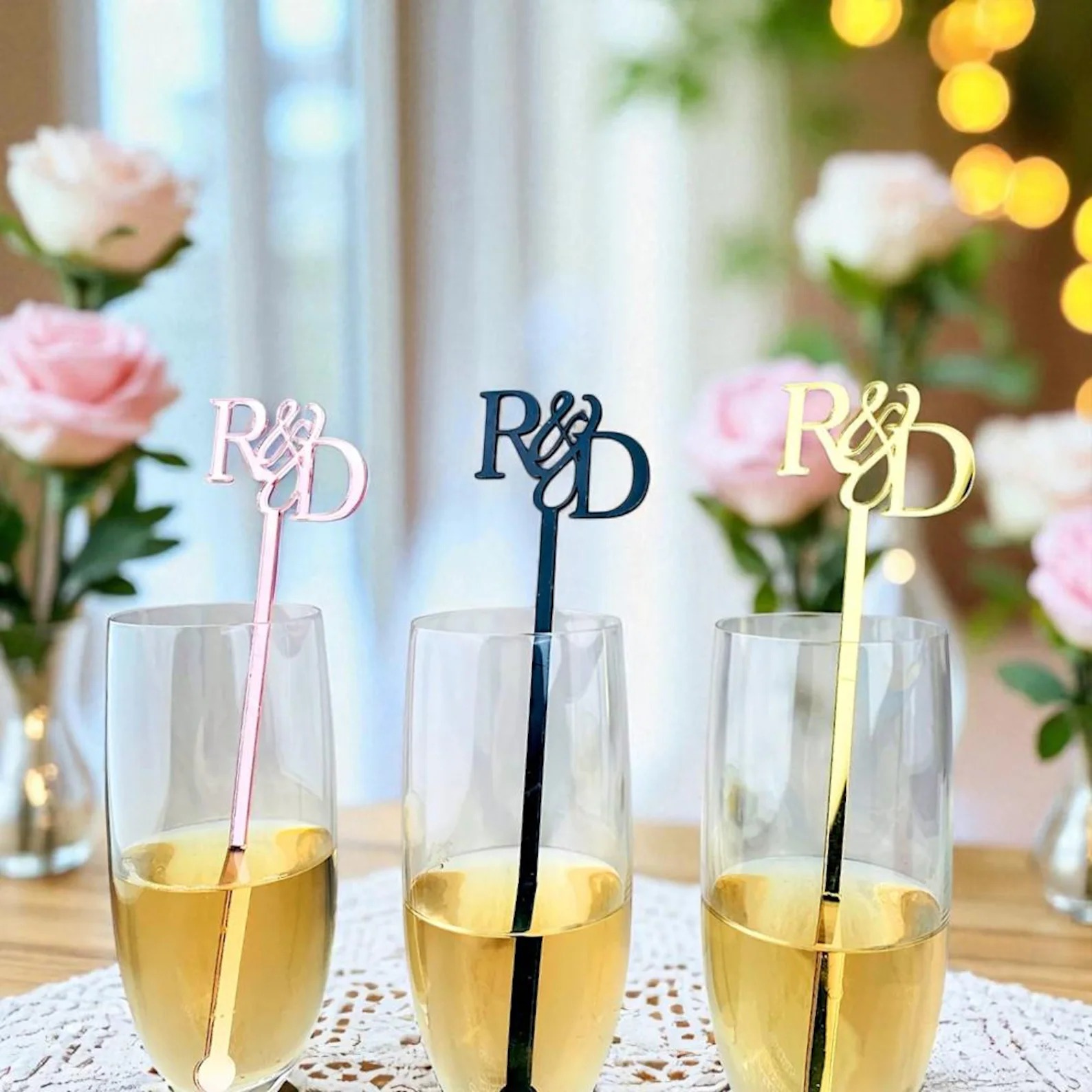 Personalized wedding drink stirrers with R&D initials in pink, black, and gold placed in champagne glasses