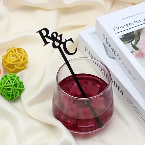 Custom black acrylic drink stirrer with "R & C" initials placed in a red cocktail glass.