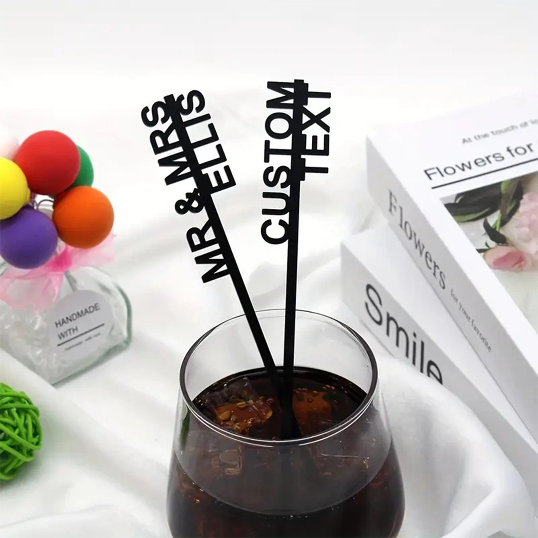 Custom black drink stirrers with personalized text used in a cocktail glass.