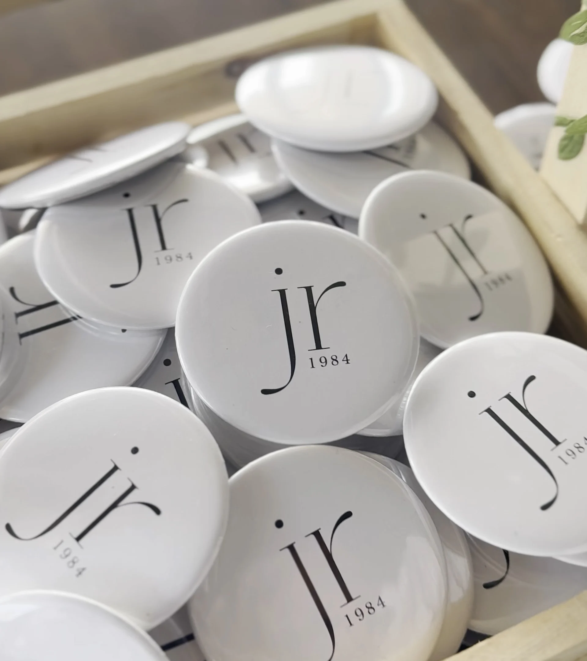 Custom white corporate logo pin badges with minimalist branding design arranged in a tray for promotional events.