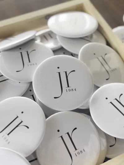 Custom white corporate logo pin badges with minimalist branding design arranged in a tray for promotional events.
