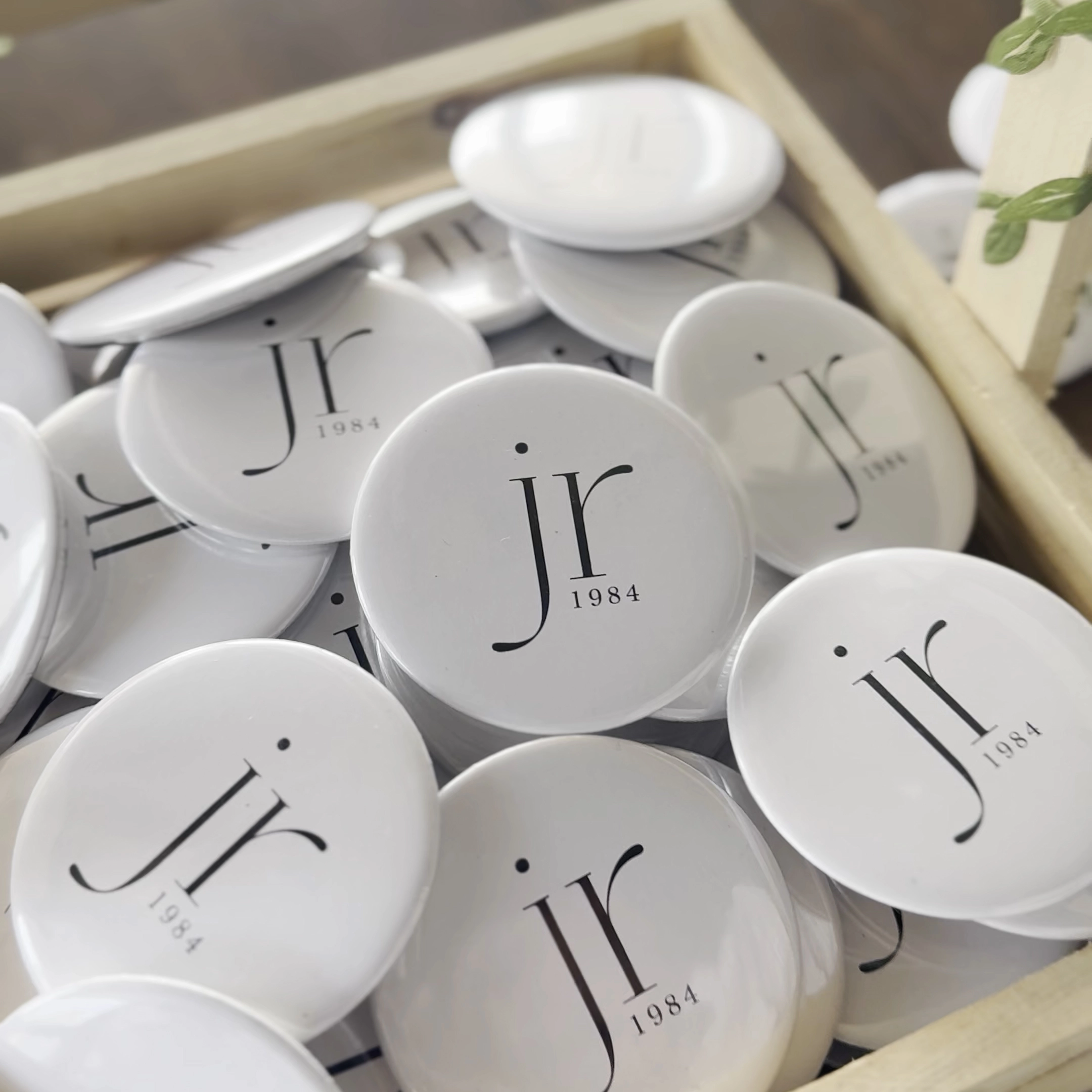 Custom white corporate logo pin badges with minimalist branding design arranged in a tray for promotional events.